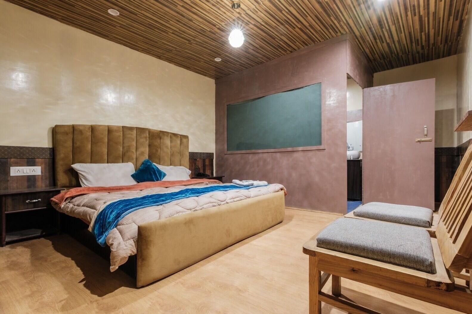 A bedroom with a bed, a nightstand, a wooden chair, a wooden desk, and a chalkboard on the wall.
