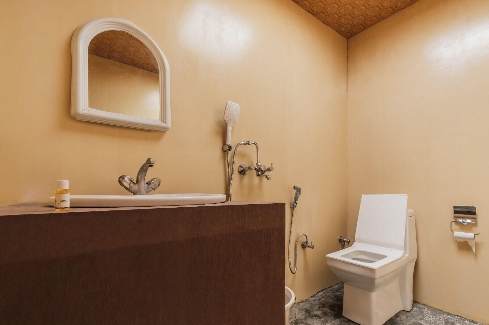 A bathroom with a wooden vanity, a white sink, a mirror, a shower head, and a toilet.