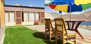 A patio with a table and chairs, a small lawn, and a building with windows and doors. - Grand Cozy Cottage Pangong (Leh)