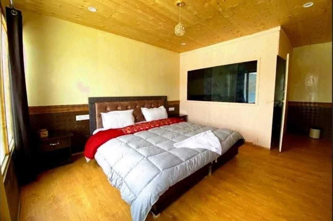 A bedroom with a bed, wooden flooring, a window, and a door.