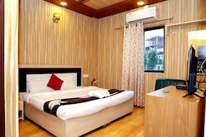 Habitación de hotel con cama, escritorio, aire acondicionado, lámpara de pared y ventana con cortinas.