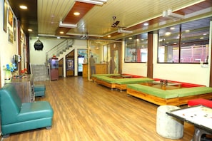 A restaurant with wooden floors, green cushioned seating, a counter, and a ceiling fan. - The Mountain View (Rishikesh)