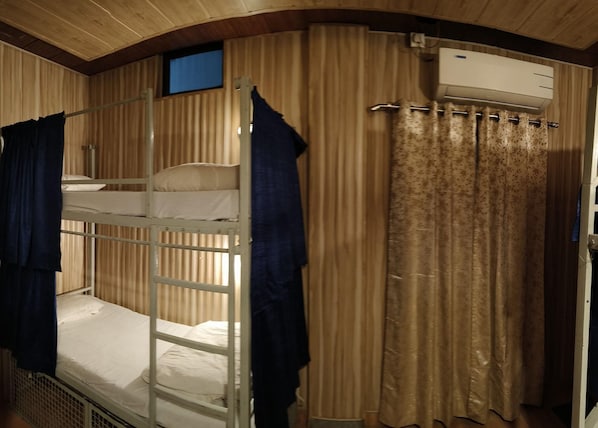 Habitación con literas, una escalera, ventana, aire acondicionado y cortina.