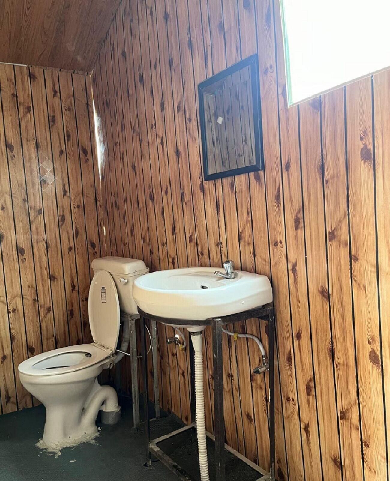 A wooden-paneled bathroom with a toilet and a pedestal sink.
