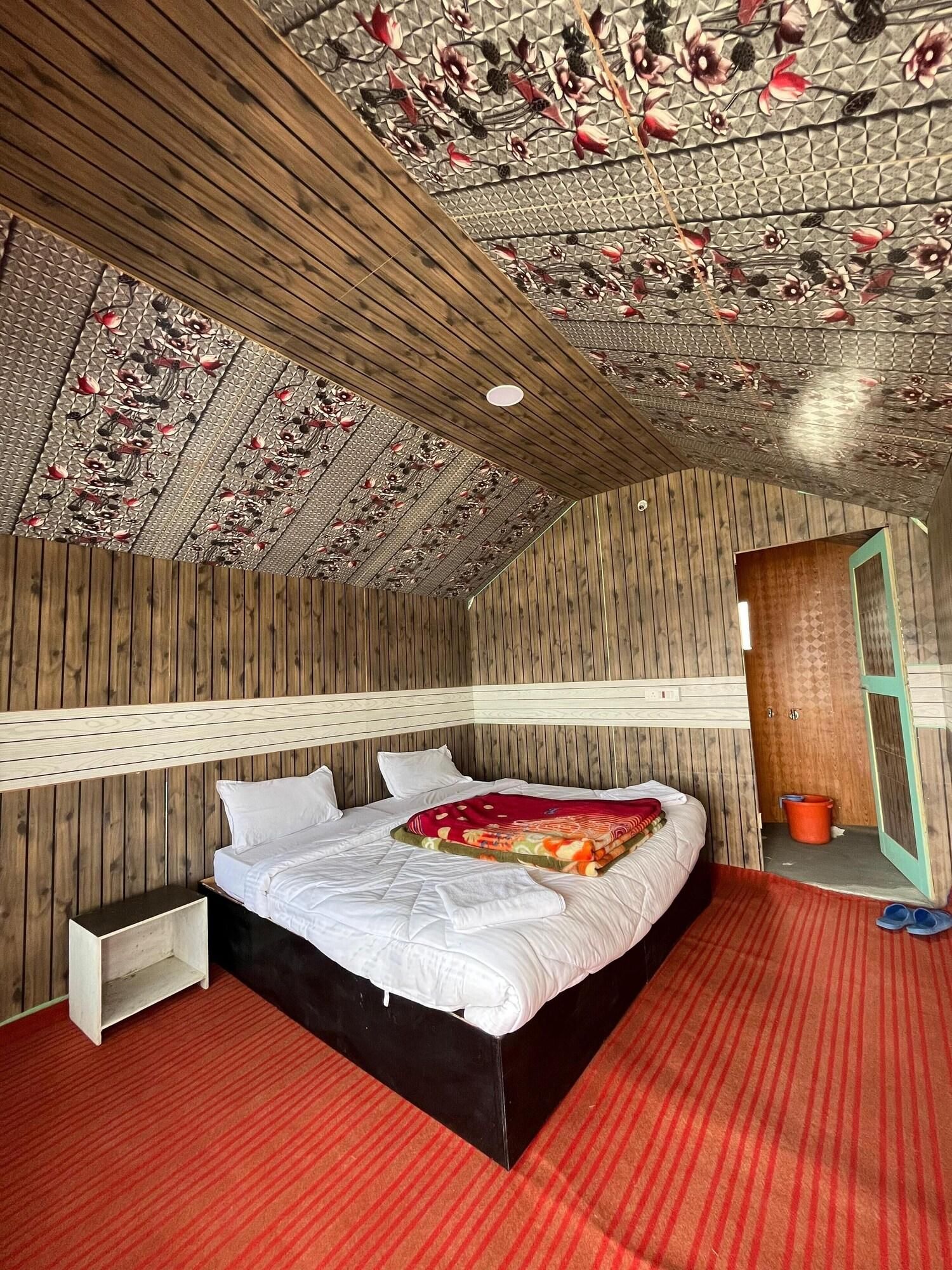 A bedroom with a wooden ceiling, a bed with white bedding, a red carpet, and a wooden nightstand.