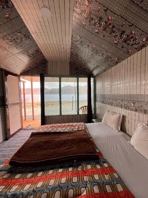 A bedroom with a large bed, a view of the outdoors, and a wooden ceiling. - Padma Cottage Pangong (Leh)