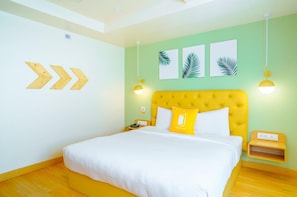 A hotel room with a yellow headboard, white bedding, a bedside table with a phone, and a wall with leaf-patterned artwork. - Bloom Hotel - Cyber Towers (Hyderabad)