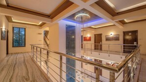 A spacious interior with a high ceiling, a central chandelier, and a staircase leading to an upper level. - Hotel Arch Inn (Jaipur)