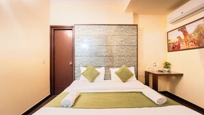 A hotel room with a bed, a nightstand, a wall-mounted air conditioner, and a painting. - Hotel Arch Inn (Jaipur)