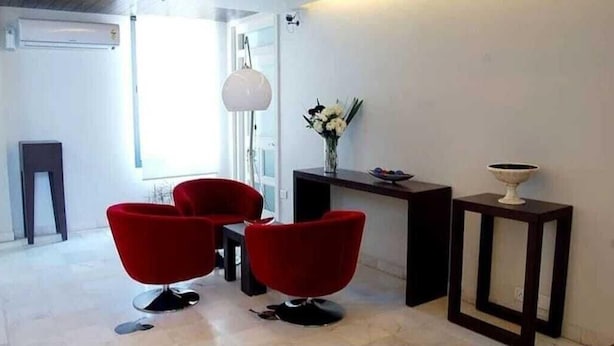 A modern living room with two red chairs, a small table, a vase with flowers, and a decorative bowl on a side table. - Hotel Arch Inn (Jaipur)