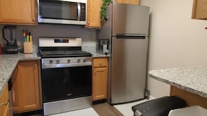 A kitchen with wooden cabinets, stainless steel appliances, a microwave, stove, refrigerator, and a trash bin. - Mid-Term Rental Furnished 2BR/2BA Condo in Germantown, MD (Germantown)