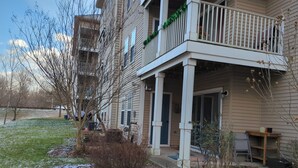 A residential building with a balcony, a covered porch, and a small garden area with some snow on the ground. - Mid-Term Rental Furnished 2BR/2BA Condo in Germantown, MD (Germantown)
