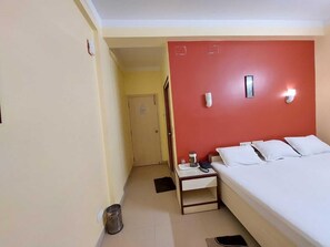 A hotel room with a bed, bedside table, lamp, and a trash bin.