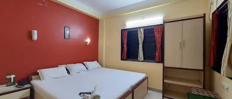 Habitación de hotel con cama, armario, ventilador de techo, ventana con cortinas y aire acondicionado instalado en la pared.