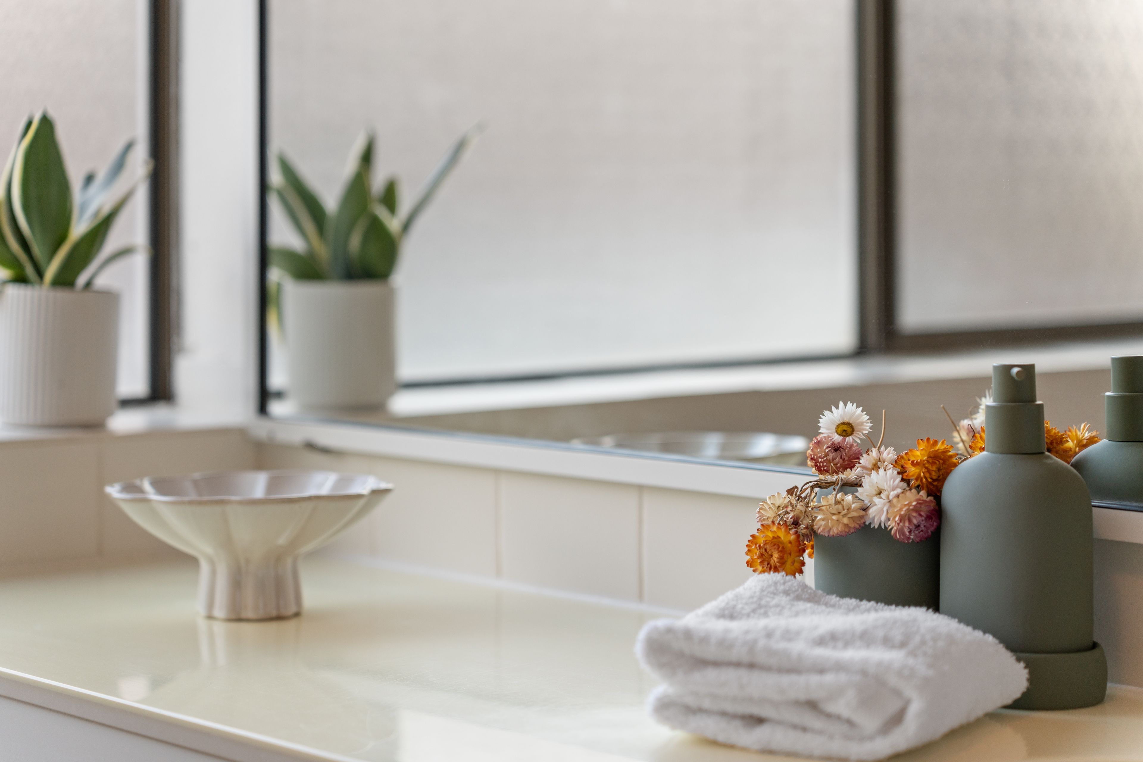 A bathroom counter with a white basin, a towel, and a vase with flowers.