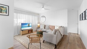 Ein Wohnzimmer mit Fernseher, Sofa und Korbsessel.