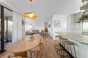 Eine moderne Küche mit einem Holztisch, Barhocker, einer großen Pendelleuchte und Blick in den Wohnbereich.