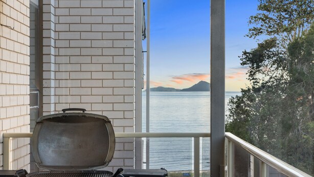 Ein Balkon mit Grill, einer Ziegelwand und Blick auf Meer und Berge.