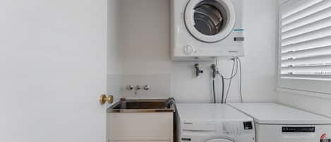 Une buanderie équipée d’un lave-linge à chargement frontal, d’un sèche-linge et d’un évier avec des robinets.