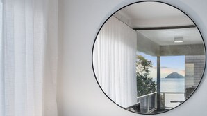 Ein Zimmer mit einem großen, runden Spiegel, der einen Balkon mit Blick auf das Meer und die Berge zeigt.
