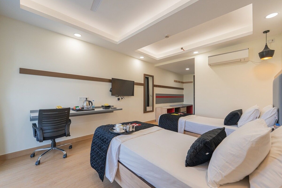 A hotel room with two beds, a desk, a chair, a TV, and an air conditioning unit.