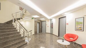 Vestíbulo con una escalera, una señal de salida de incendios, un mostrador de recepción y una puerta con el número 102.