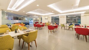 Un área de comedor moderna con varias mesas y sillas, ventanas amplias e iluminación empotrada en el techo.