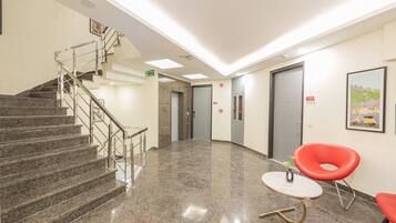 A lobby with a staircase, a fire exit sign, a reception desk, and a door marked with the number 102.