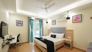 A hotel room with a bed, desk, chair, desk lamp, ceiling fan, artwork, and a window with curtains. - Mastiff City Nest Golf Course Extension by Othpl (Gurugram)