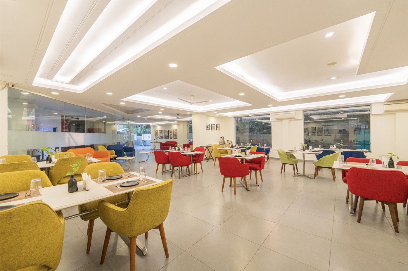 A modern dining area with multiple tables and chairs, large windows, and recessed ceiling lighting.