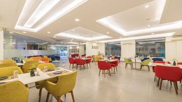 A modern dining area with multiple tables and chairs, large windows, and recessed ceiling lighting.