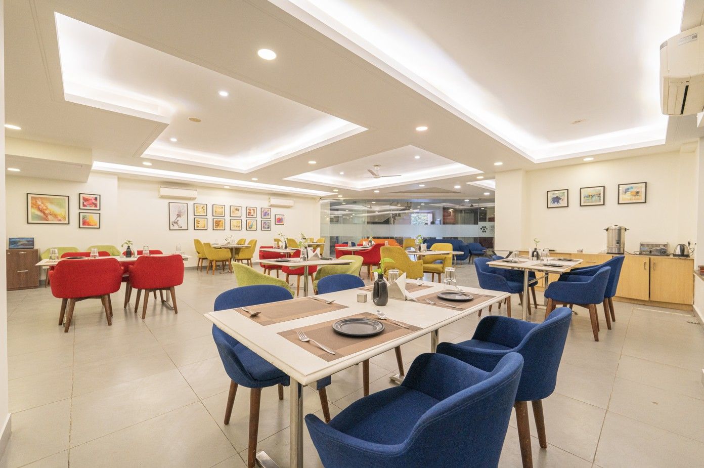 Un comedor amplio con varias mesas y sillas, un área de cocina y obras de arte enmarcadas en las paredes.
