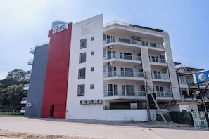 Un edificio de varios pisos con fachada roja y blanca, balcones y unidades de aire acondicionado.
