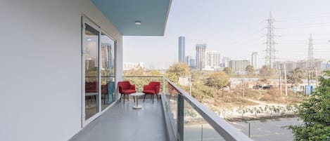 A balcony with a city view, red chairs, and a glass door leading to a room.