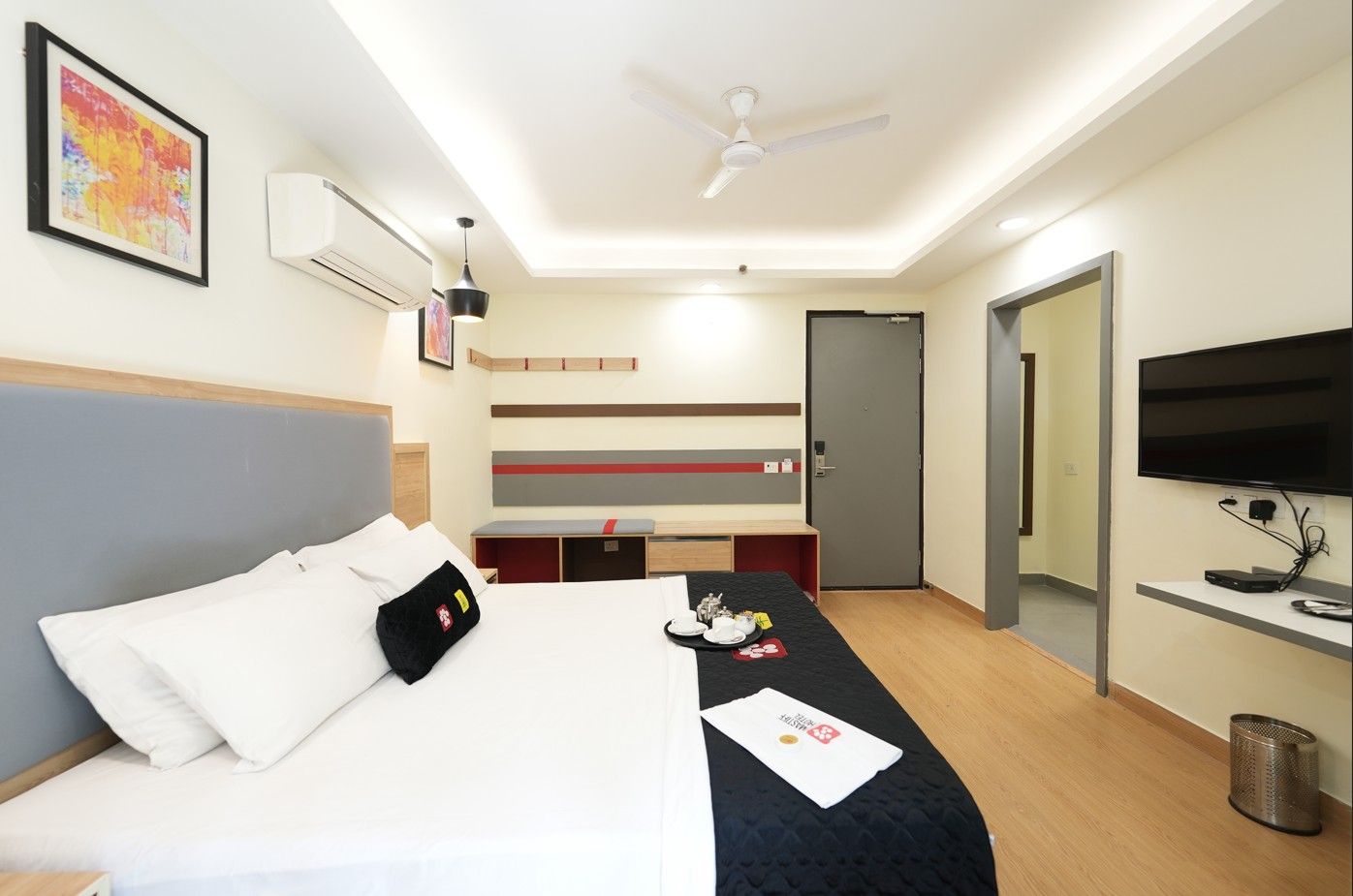 Een hotelkamer met een bed, een bureau, een televisie en een plafondventilator.