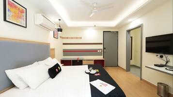 Een hotelkamer met een bed, een bureau, een televisie en een plafondventilator.
