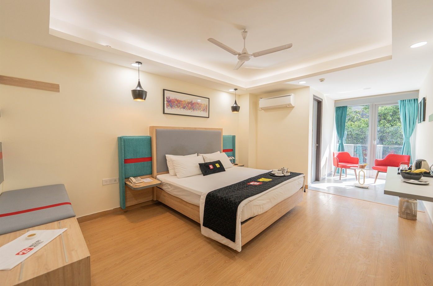 A modern hotel room with a bed, bedside tables, a desk, chairs, a ceiling fan, and a large window with curtains.