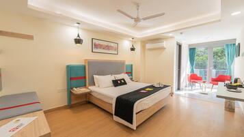 A modern hotel room with a bed, bedside tables, a desk, chairs, a ceiling fan, and a large window with curtains.