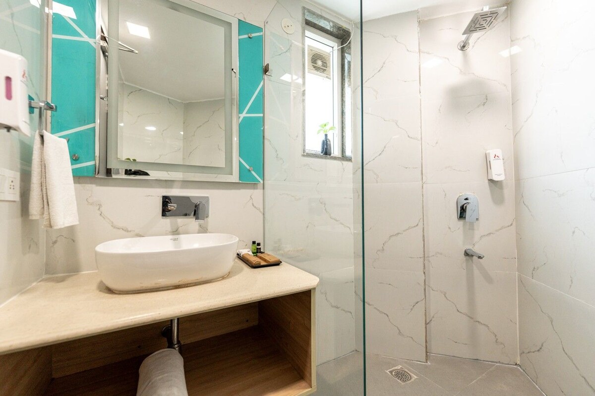 A bathroom with a large white sink, a glass shower enclosure, and a mirror with a teal accent wall.