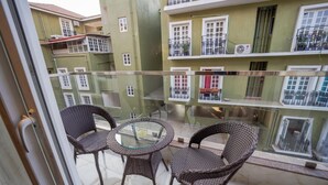 A balcony with wicker chairs and a glass table, overlooking a building with multiple balconies and windows. - Casa De Katson (Alto de Porvorim)