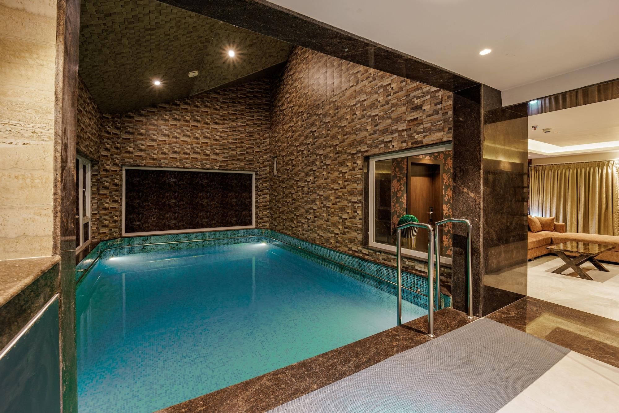 A swimming pool with a stone wall, a glass door, and a lounge area with a sofa and a coffee table.