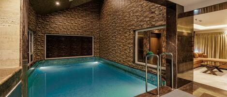 A swimming pool with a stone wall, a glass door, and a lounge area with a sofa and a coffee table.