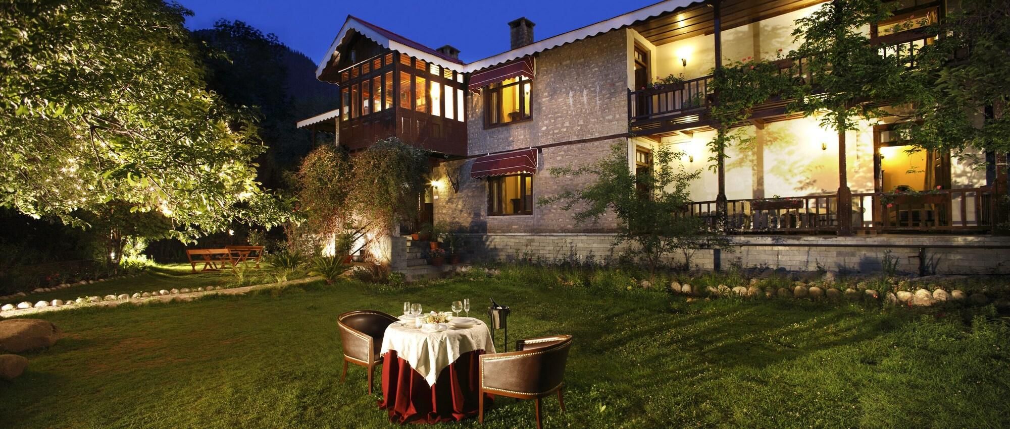 Un bâtiment en pierre de deux étages, avec un espace repas aménagé à l’extérieur, comprenant une table avec des chaises et une nappe blanche.