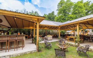 An outdoor patio area with wooden furniture, a bar, and a fire pit. - Bedzzz Xclusiv Baikunth Manali By Leisure Hotels (Manali)