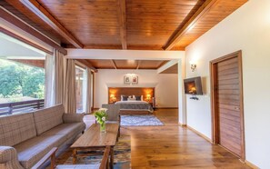Une pièce avec un plafond en bois, un canapé, une table ornée d’un vase de fleurs, un lit avec une tête de lit et un téléviseur fixé au mur.