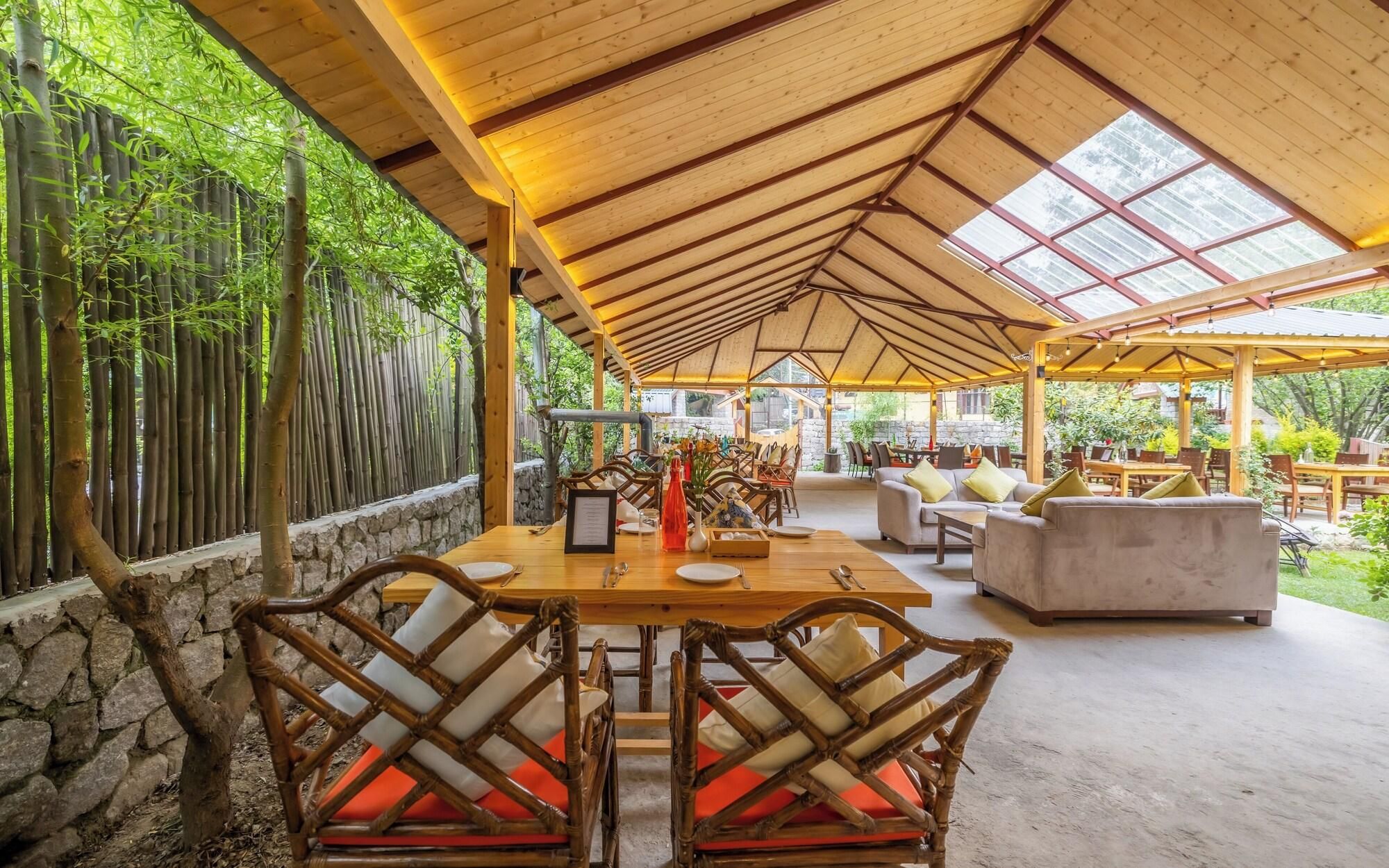 An outdoor covered dining area with bamboo walls, stone walls, and a variety of seating including tables and chairs.