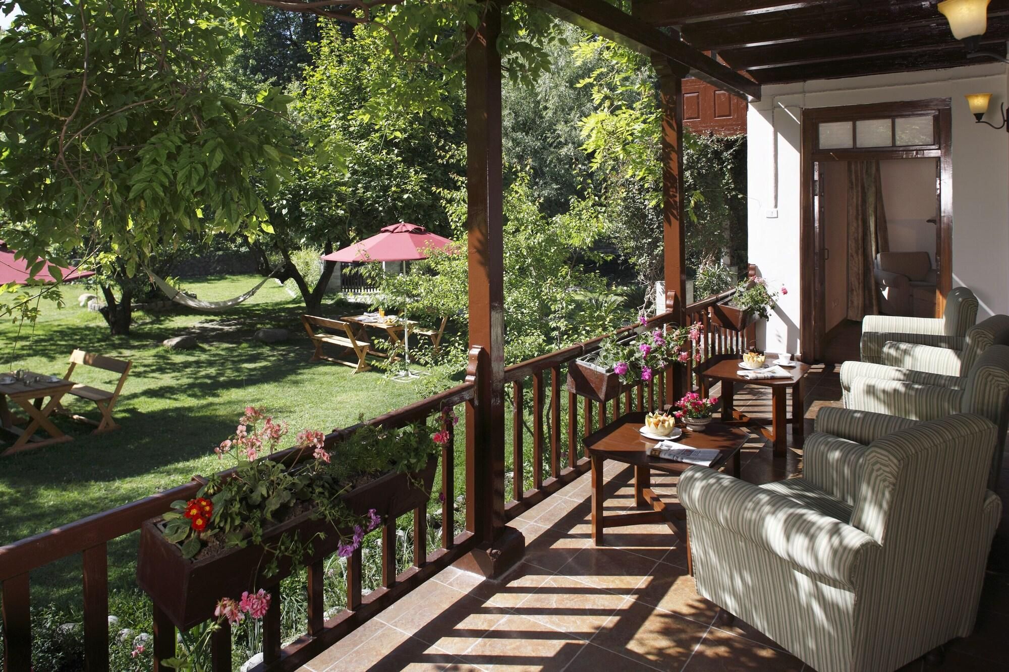 A covered outdoor seating area with a wooden deck, a table with chairs, and a view of a lush garden.