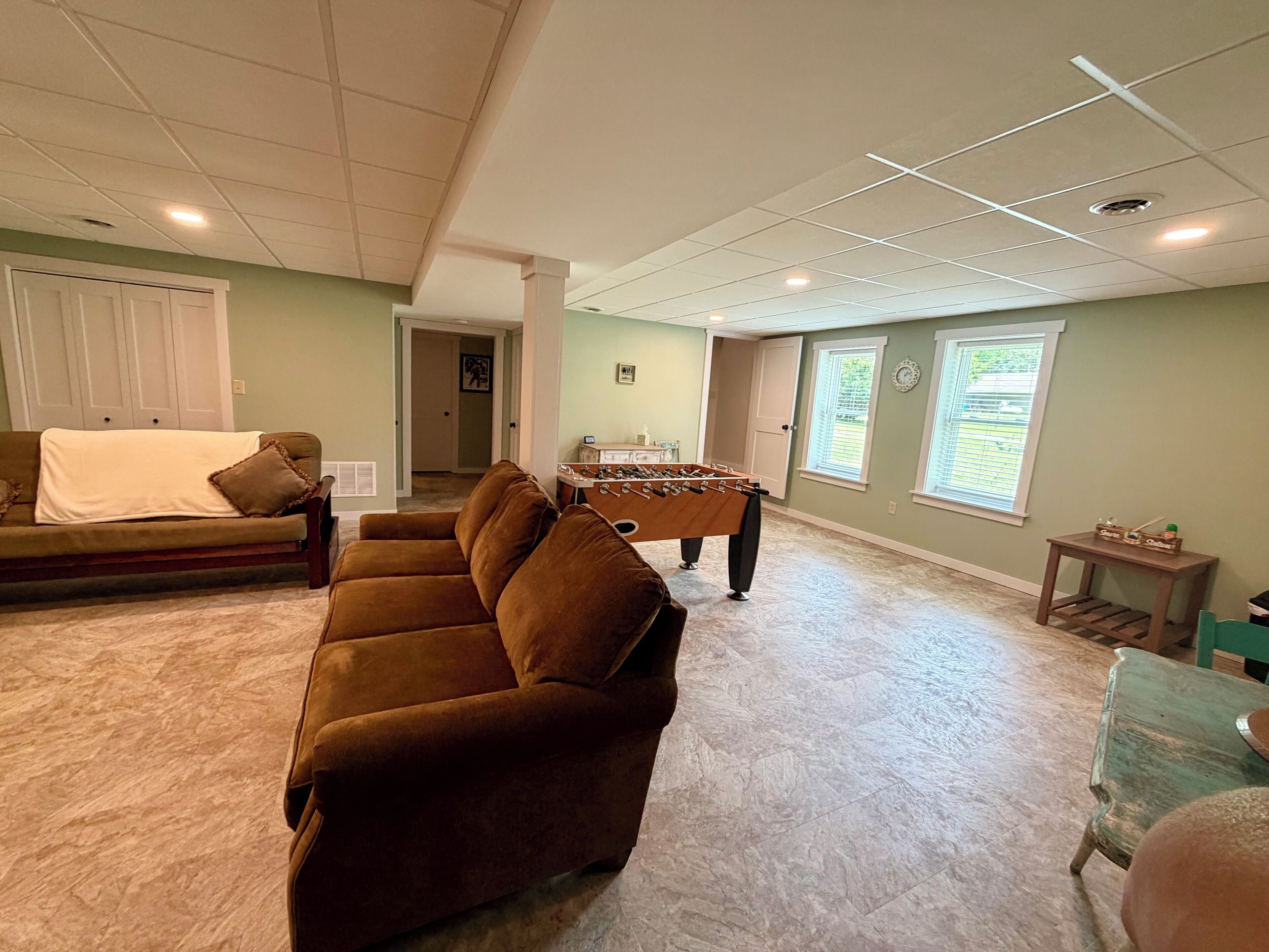 A living room with a brown sofa, a foosball table, and a window with blinds.