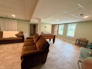 Ein Wohnzimmer mit braunem Sofa, einem Kicker und einem Fenster mit Jalousien.