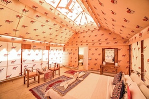 A camel-themed room with a bed, chairs, a table, and a mirror. - Lakhmana Desert Camp (Jaisalmer)